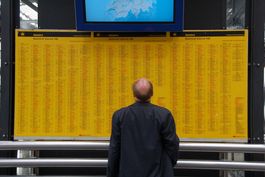 Mann im Bahnhof schaut auf ausgehängten Fahrplan auf gelbem Papier
